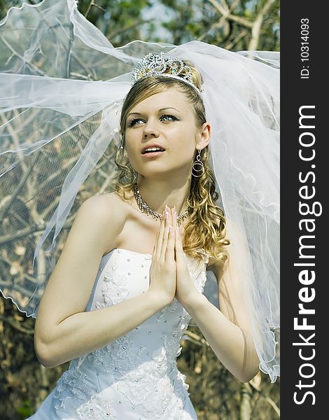 Praying bride wearing crown, outdoors shot.