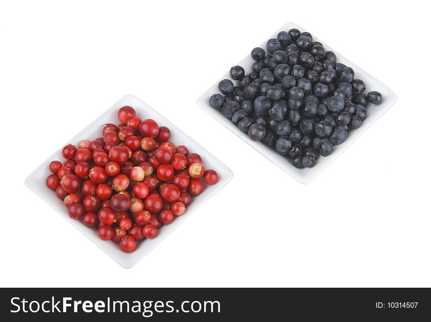 Ripe bilberries and cranberries in saucers on white background.