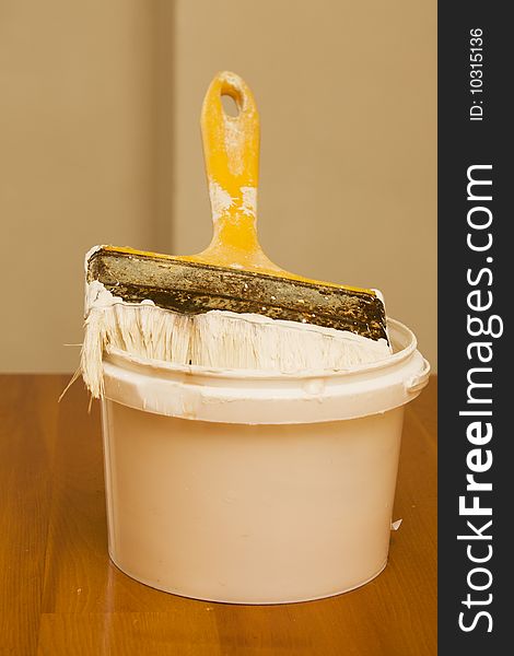 Paintbrush and bucket with paint on wooden table