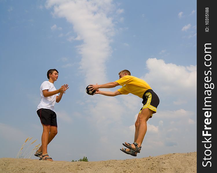 Two boys play a ball on sand