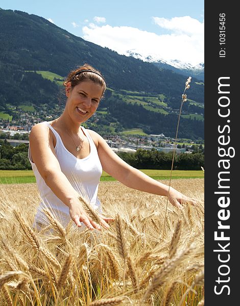 A young woman in the yellow field under blue sky in a rural alpine setting. Village in the background. Focus is on the woman. A young woman in the yellow field under blue sky in a rural alpine setting. Village in the background. Focus is on the woman.