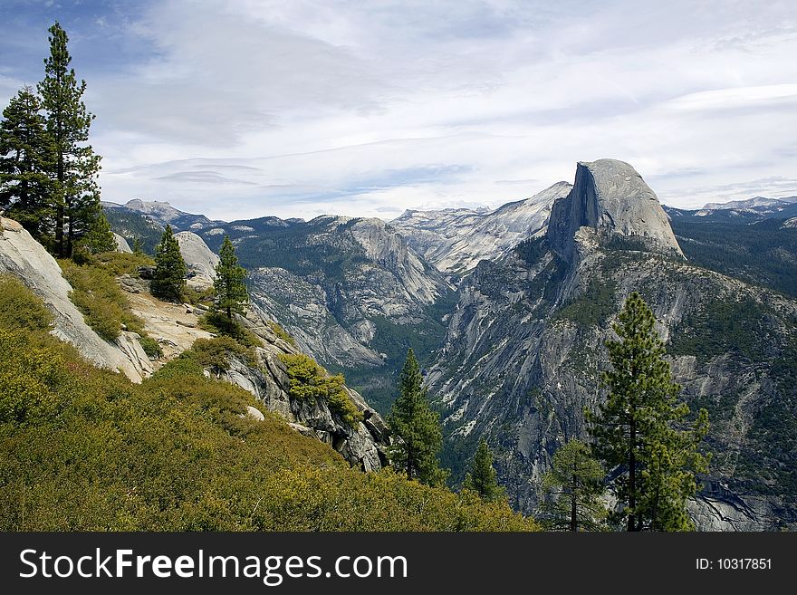 View of Half Dome with Mountains in the background and trees in the foreground. View of Half Dome with Mountains in the background and trees in the foreground