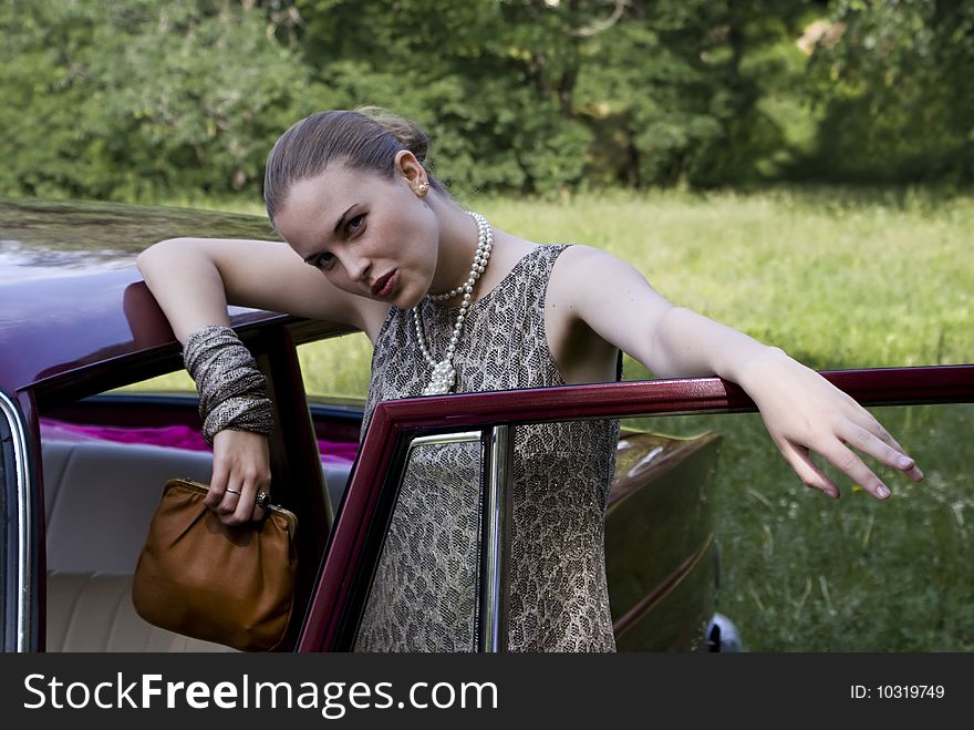 Beautiful girl at the car on a green wood background