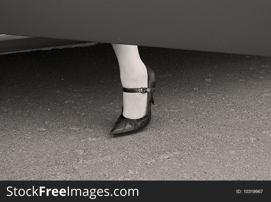 Female leg in a high heel shoe at a car door. Grayscale image