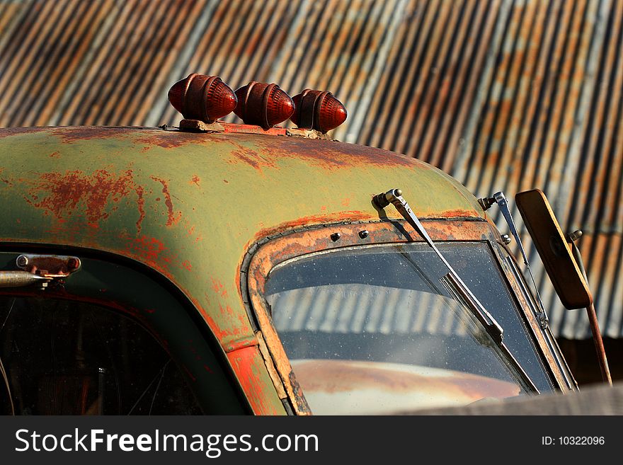 Close-up of old antique truck in front of rusty corrugated roofing in background.