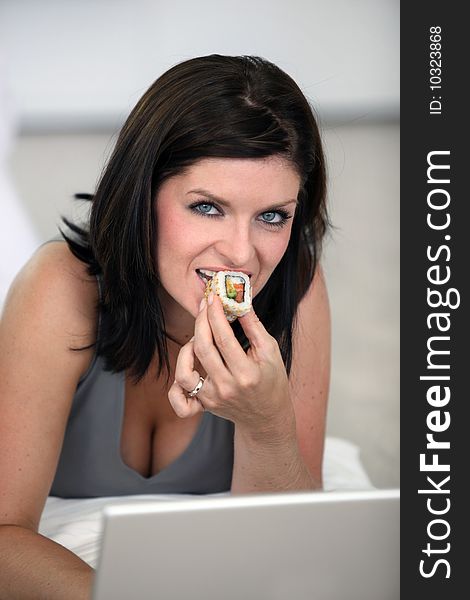 Happy young woman eating sushi with chopsticks