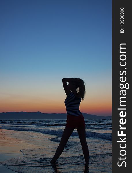 Silhouette of a young woman standing on a beach at sunset. Shot from behind. Silhouette of a young woman standing on a beach at sunset. Shot from behind.