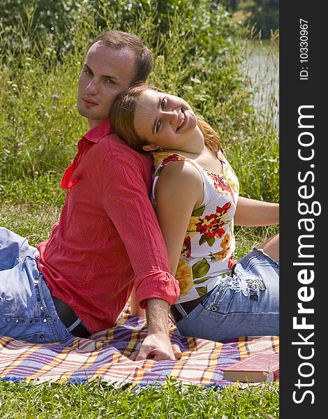 Romantic couple is sitting on the plaid. Portrait of a happy couple at the park on vacation. Charming young girl and boy spending quality time.