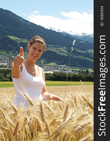 A young woman in the yellow field under blue sky in a rural alpine setting. Village in the background. Focus is on the woman. A young woman in the yellow field under blue sky in a rural alpine setting. Village in the background. Focus is on the woman.