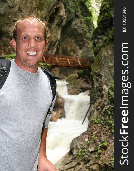 Young man is hiking on a trail in the mountains. A big waterfall in the background - focus on the young man. Young man is hiking on a trail in the mountains. A big waterfall in the background - focus on the young man.