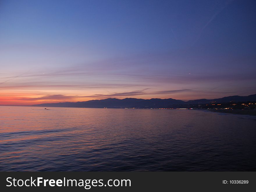 Beautiful sunset on the beach with mountains and city lights
