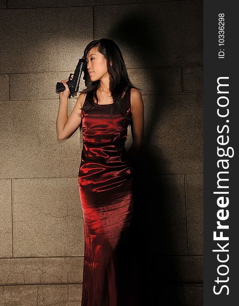 Beautiful young Asian woman in red dress with a gun in an underground tunnel. Beautiful young Asian woman in red dress with a gun in an underground tunnel.
