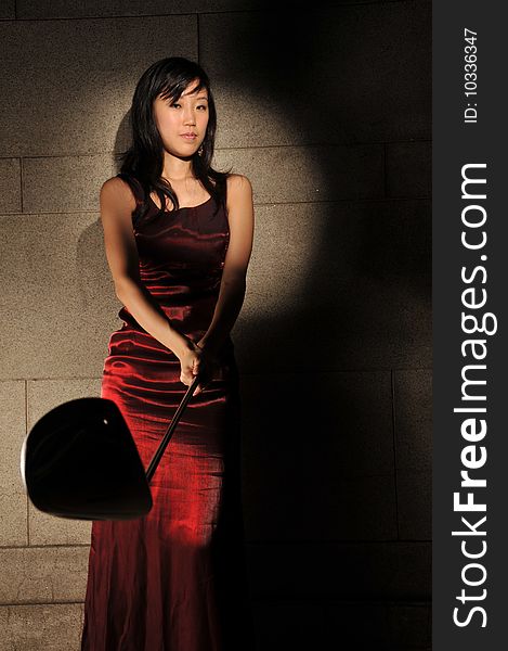 Beautiful young Asian woman in red dress holding a golf stick in an underground tunnel. Beautiful young Asian woman in red dress holding a golf stick in an underground tunnel.