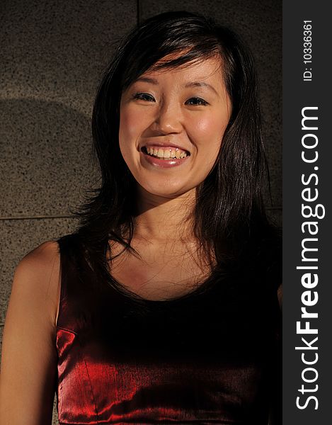 Beautiful young Asian woman in red dress standing against the wall.