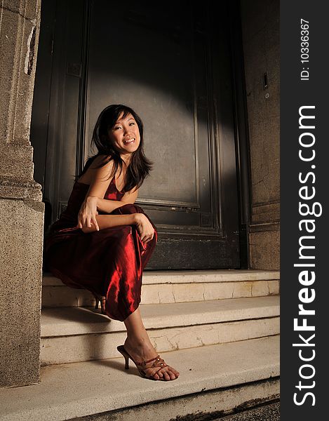 Beautiful young Asian woman in red dress sitting at the steps.