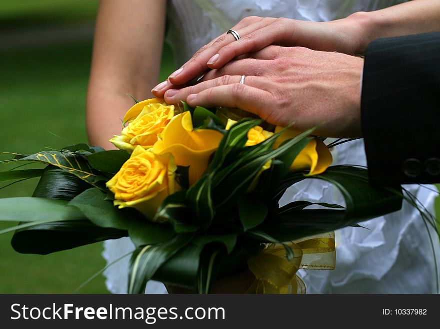 Hands of bride and groom over yellow rose bouquet. Hands of bride and groom over yellow rose bouquet