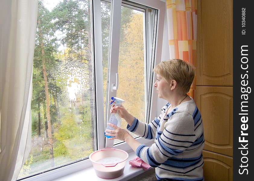 The woman washing a window. Behind a window trees are visible. Autumn.