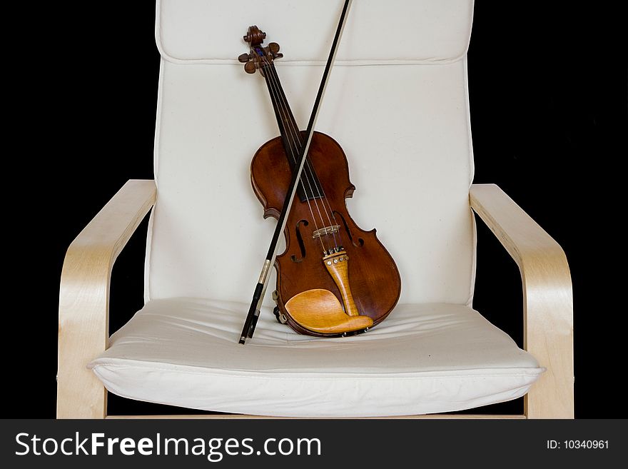 Old violin resting on a chair isolated over a black background