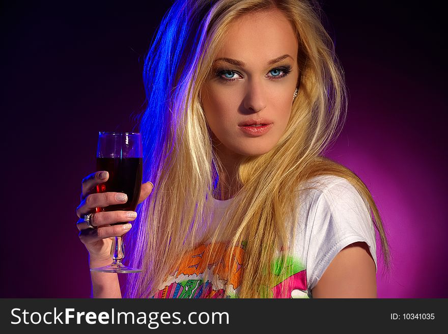 Portrait of a beautiful blonde with green eyes and a glass of wine in their hands on purple background. Portrait of a beautiful blonde with green eyes and a glass of wine in their hands on purple background