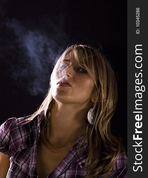 Young woman smoking against dark background