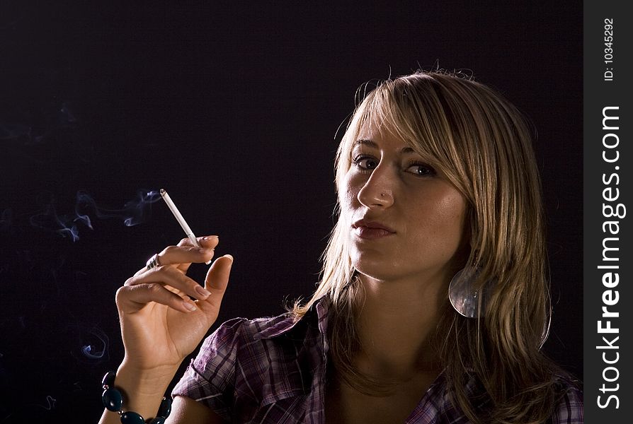 Young woman smoking against dark background