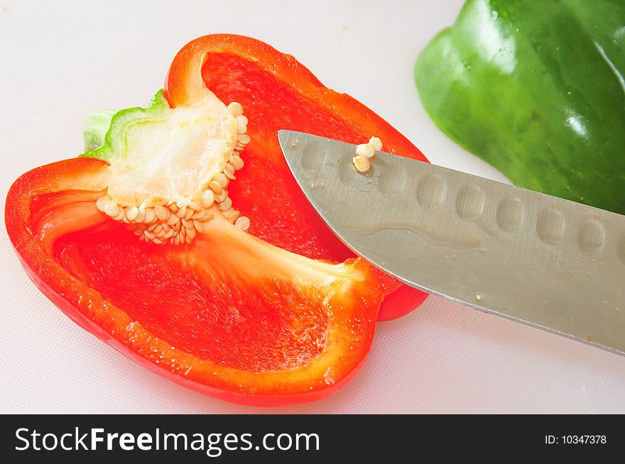 An image of a red bell and a green bell pepper cut in half on a white cutting board. An image of a red bell and a green bell pepper cut in half on a white cutting board.