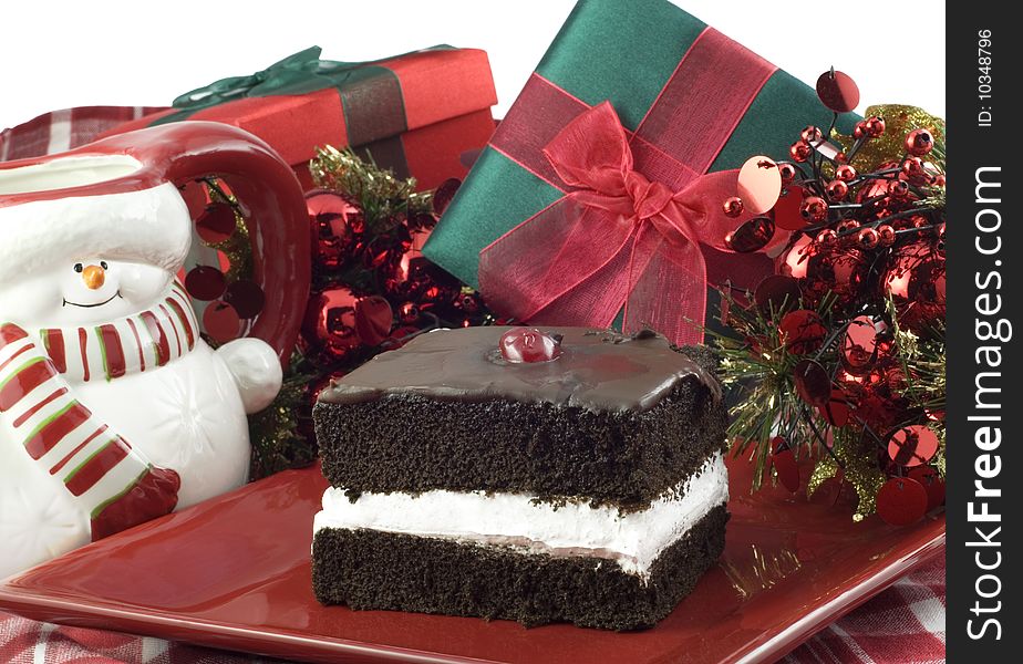 A piece of Chocolate Layer Cake on a red plate with holiday decorations, horizontal with white background and copy space. A piece of Chocolate Layer Cake on a red plate with holiday decorations, horizontal with white background and copy space