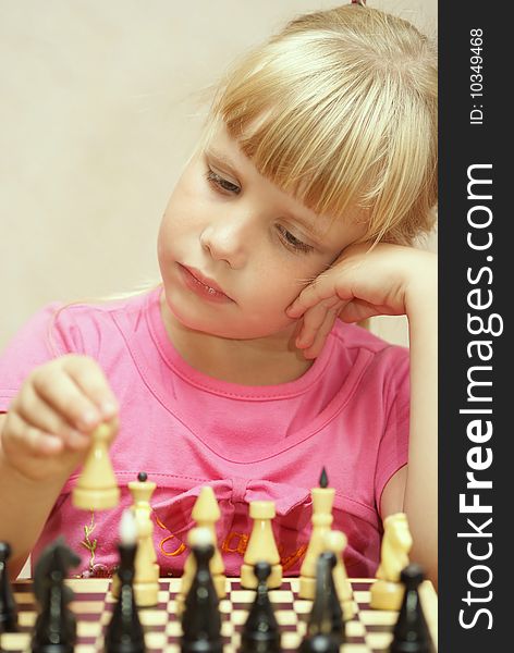 The girl in a pink dress plays a chess