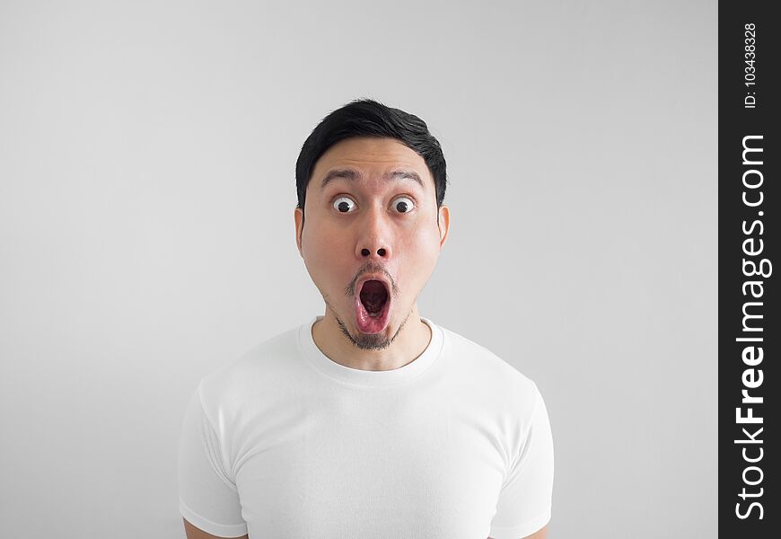 Shocked face of Asian man in white shirt on grey background.