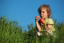 Girl Eats Red Apple In Grass Against Blue Sky Royalty Free Stock Image