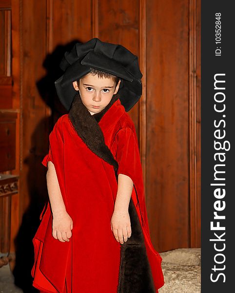 Serious cute little boy in medieval costume standing on wooden background