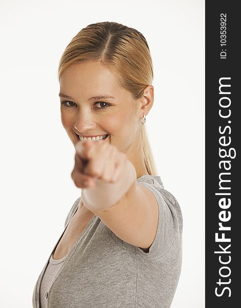 Young woman pointing at camera with selective focus on white seamless background