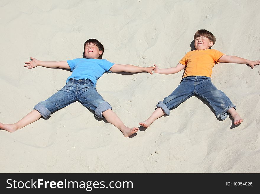Two children lying nearby on sand, summer