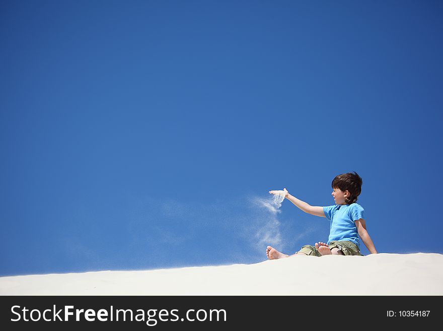 Boy Sits On Sand And Scatters It