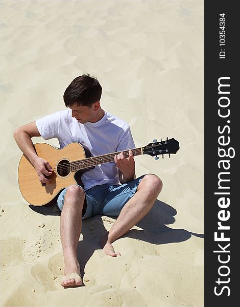 Guy plays guitar sitting on sand, summer day