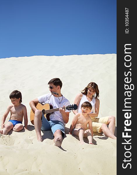 Guy in sunglasses plays guitar and  lip accordion  with children and girl sitting on sand. Guy in sunglasses plays guitar and  lip accordion  with children and girl sitting on sand