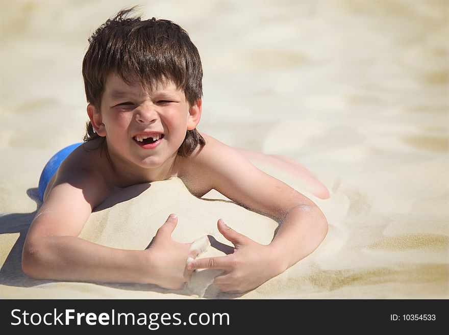 Boy without  foreteeth lies on sand, summer day