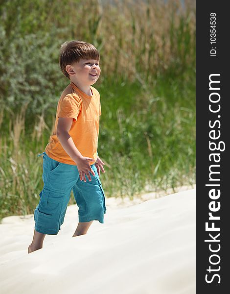 Boy goes on sand,  side view, summer day