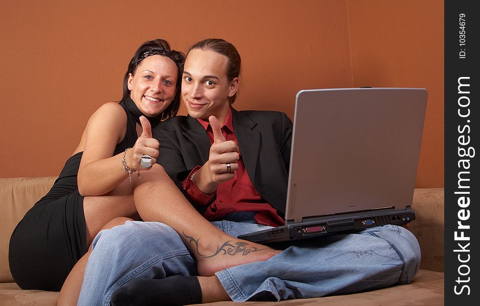 Young couple on the couch surfing the web with their laptop - showing a thumbs up sign. Young couple on the couch surfing the web with their laptop - showing a thumbs up sign.