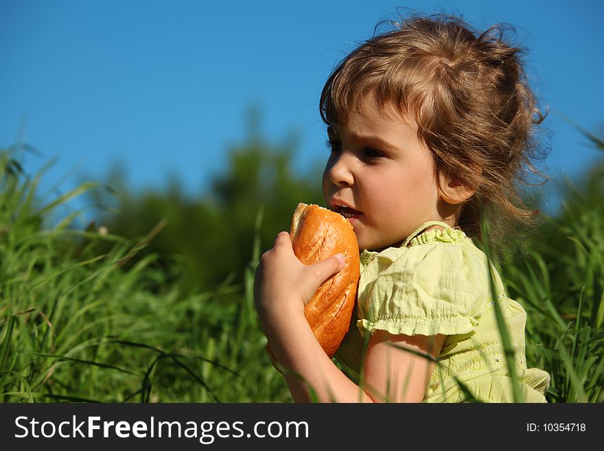 Girl eats bread in grass against blue sky