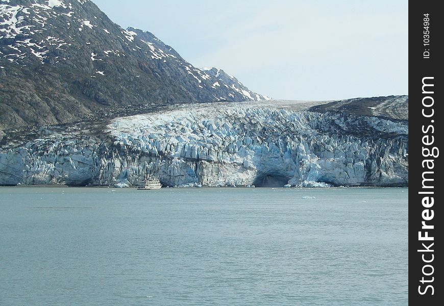 Lamplugh Glacier in Glacier Bay Alaska.  Tourist boat in front of glacier gives perspective to size of glacier and internal waterfall seen falling from the glacier to the right of the boat.