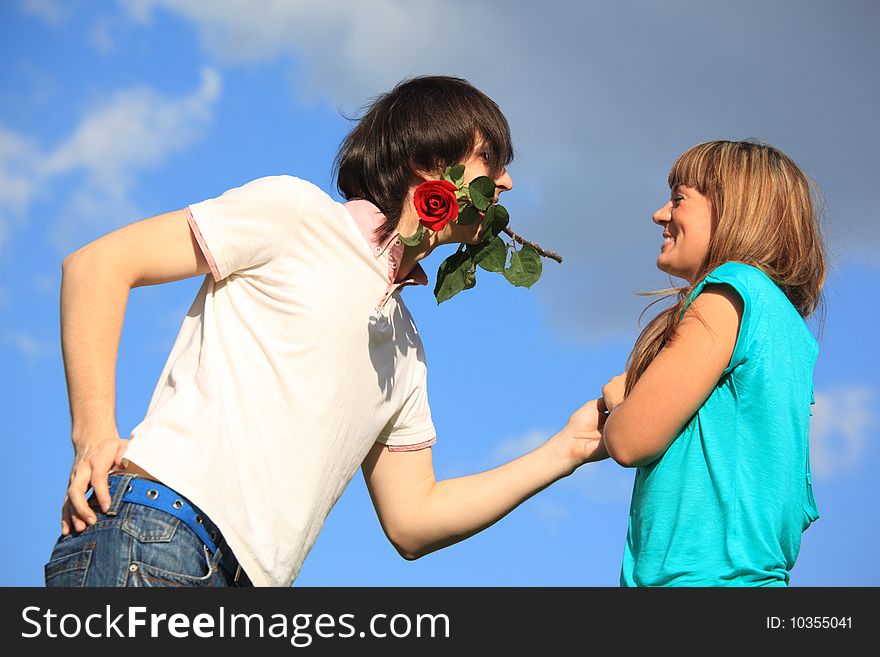 Guy with rose in mouth and smiling girl against sky. Guy with rose in mouth and smiling girl against sky