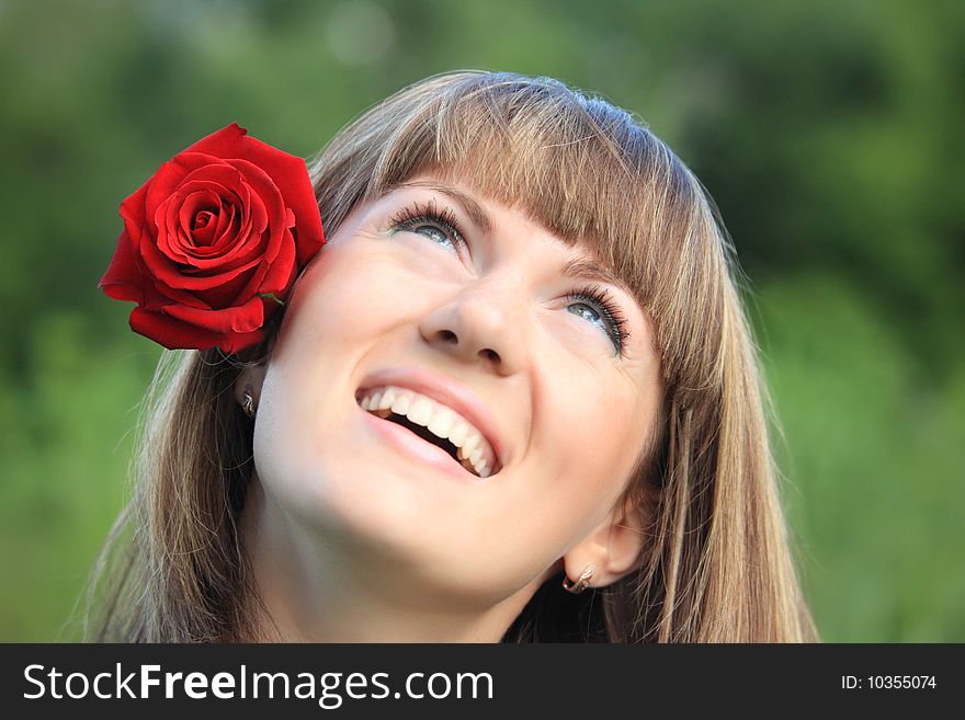 Girl with red rose in hair looks upwards