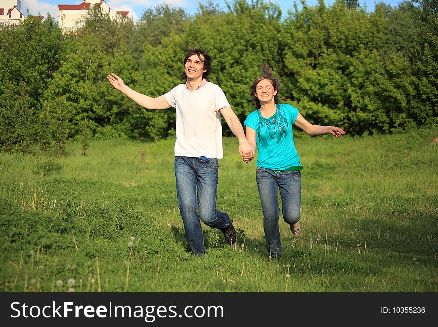 Smiling young pair runs, keeping for hands, on grass in park. Smiling young pair runs, keeping for hands, on grass in park