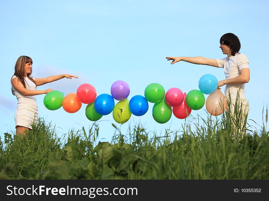 Girl and guy hold garland of multicoloured balloons in grass against sky. Girl and guy hold garland of multicoloured balloons in grass against sky