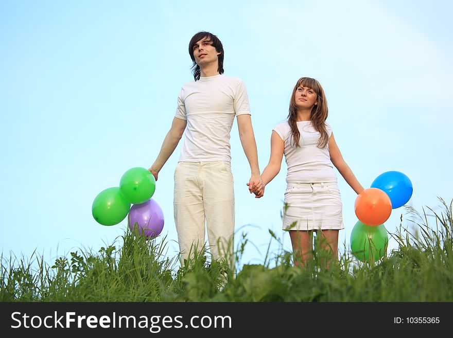 Girl and guy stand in grass with multicoloured balloons in hands. Girl and guy stand in grass with multicoloured balloons in hands
