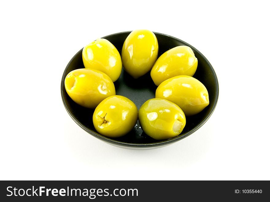 Green olives in a small round black bowl on a white background. Green olives in a small round black bowl on a white background