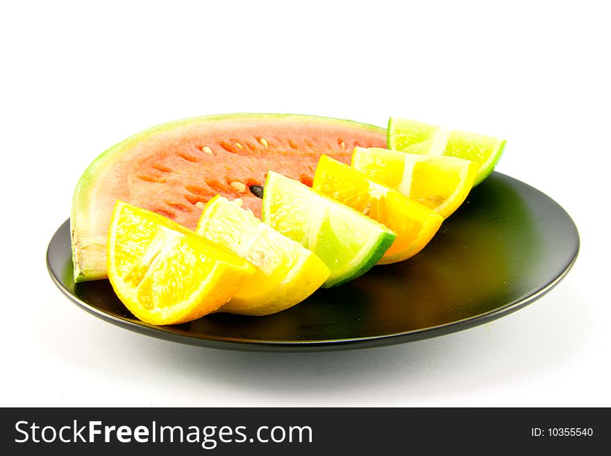 Slice of juicy red watermelon with lemon, lime and orange wedges on a black plate with a white background. Slice of juicy red watermelon with lemon, lime and orange wedges on a black plate with a white background