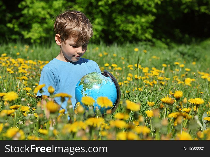 Boy with globe on meadow among blossoming dandelions