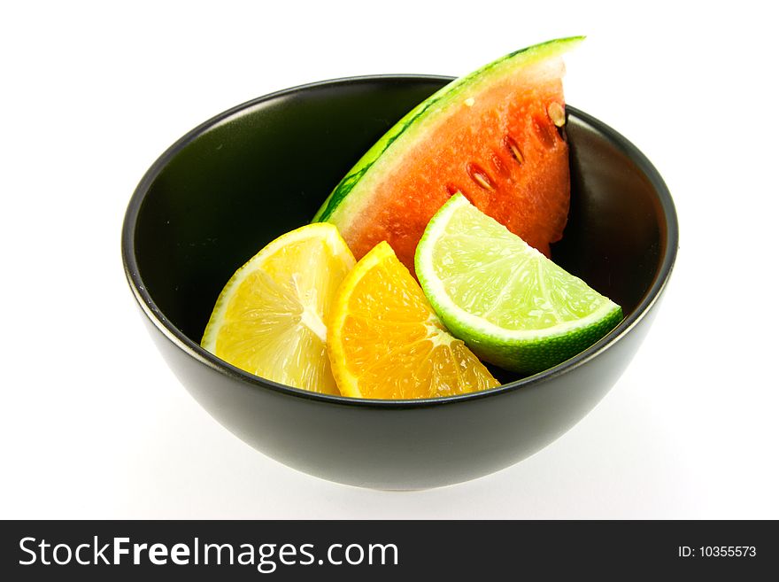 Wedges of lemon, lime and orange in a small black dish with a slice of juicy watermelon on a white background. Wedges of lemon, lime and orange in a small black dish with a slice of juicy watermelon on a white background